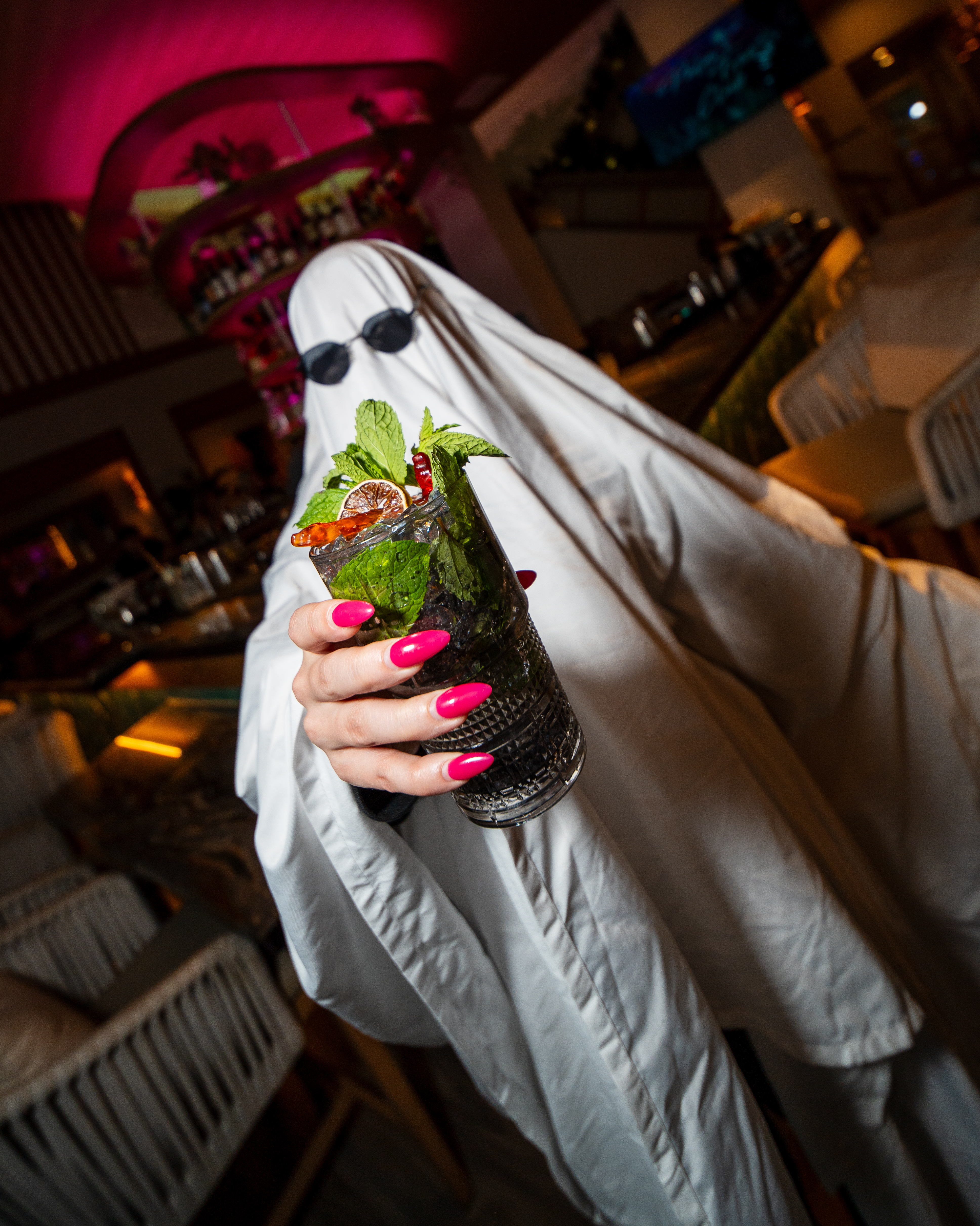 A person dressed in a ghost costume holding a cocktail at Palm Tree.