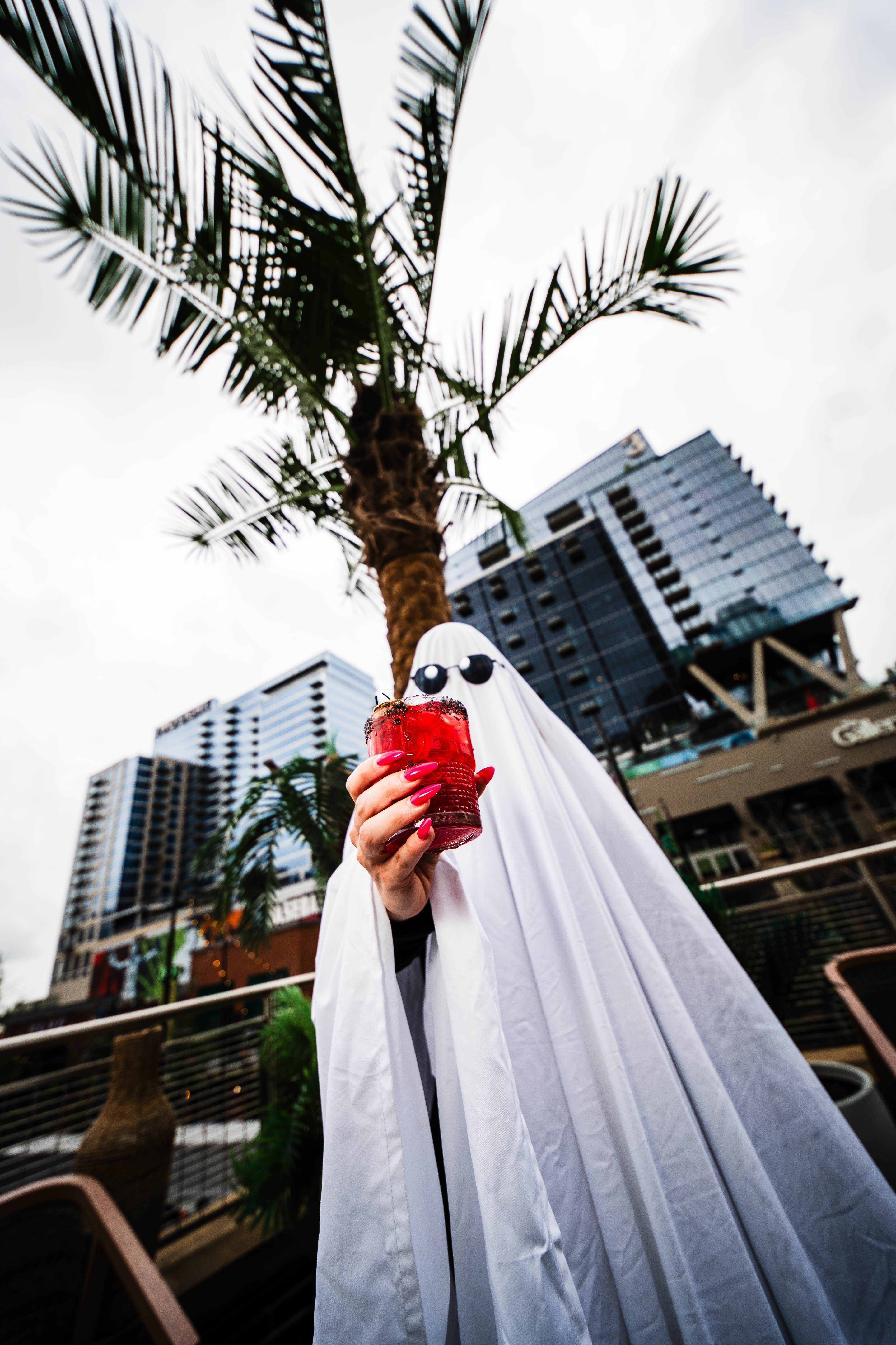 A person dressed in a ghost costume holding a cocktail at Palm Tree.
