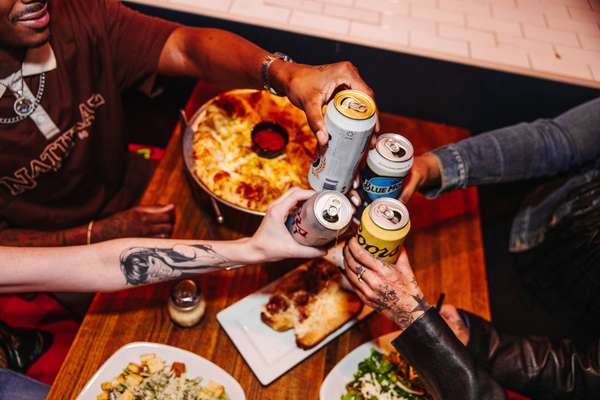 Four hands cheering cans of beer at a table