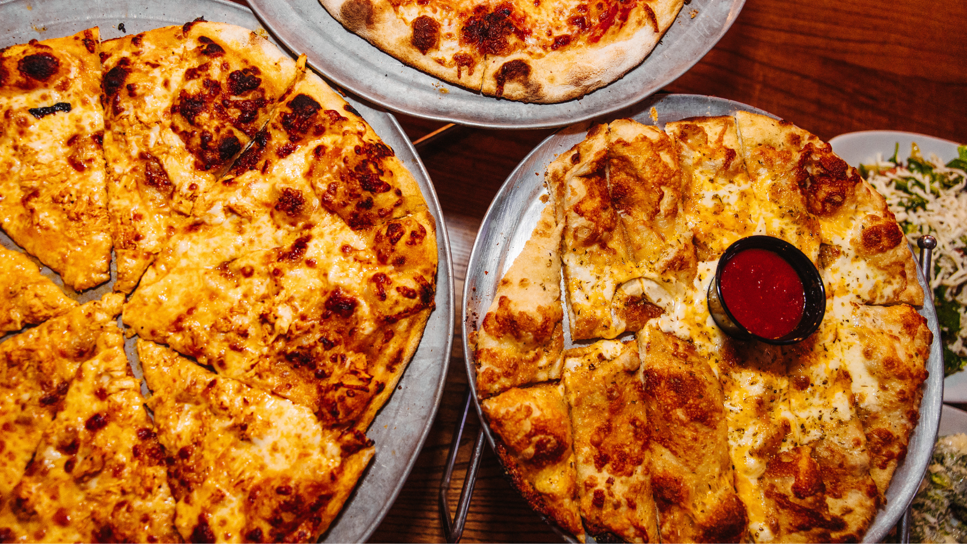 Cheese pizza and cheesy bread on metal trays on a table
