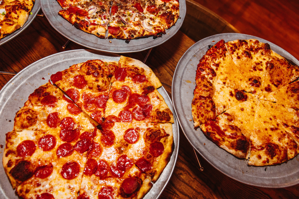 Pepperoni, cheese, and supreme pizzas on metal trays on a wood table