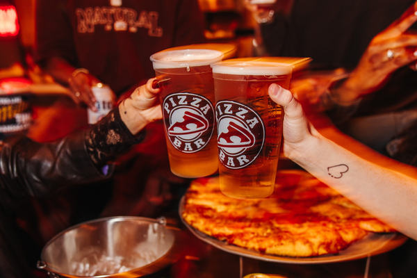 Two hands cheering beers in Pizza Bar cups with food in the background