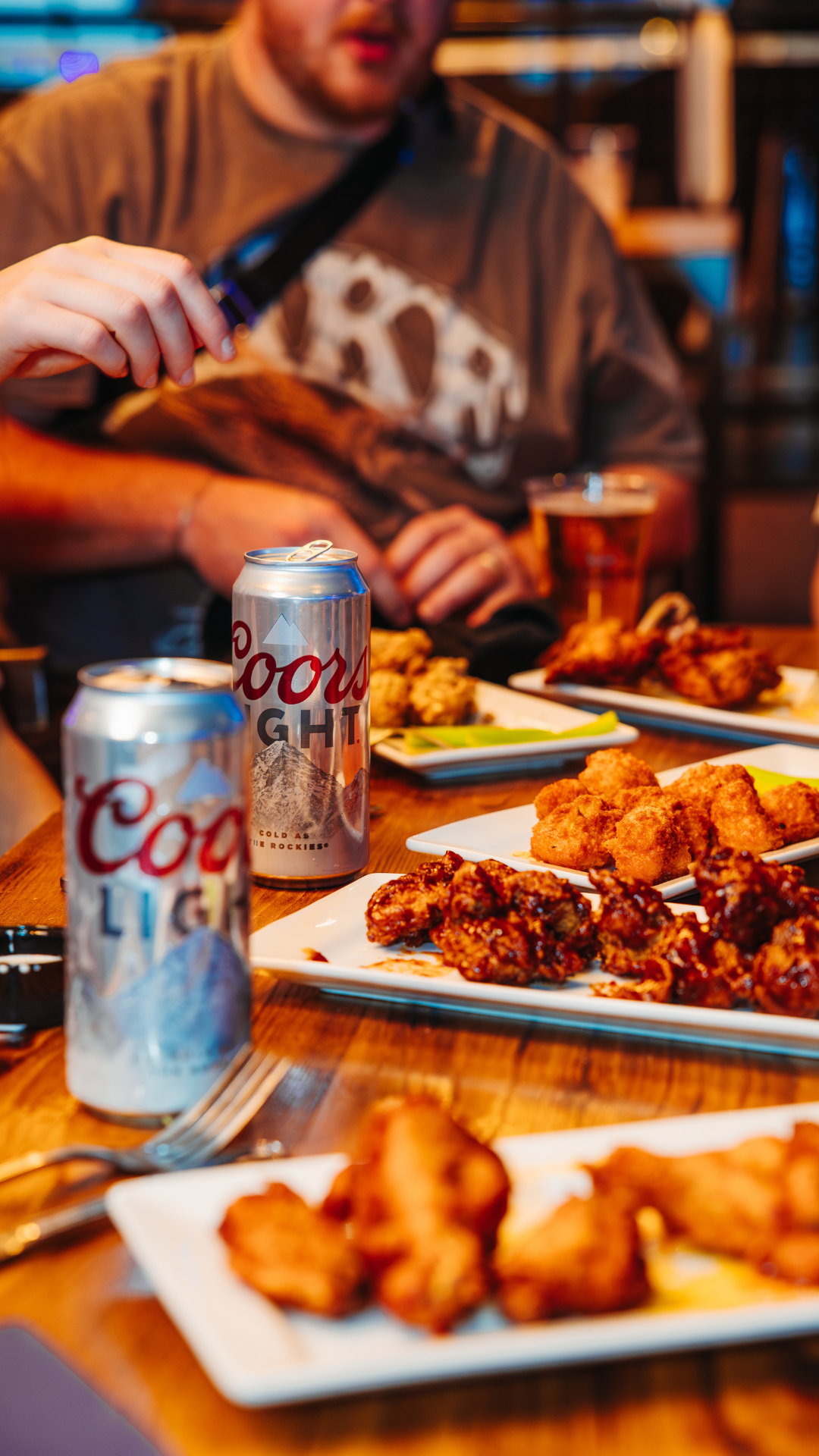 Plates of wings and cans of Coors Light on table