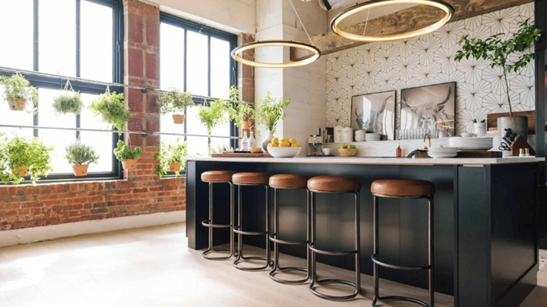 The loft residence of the cast of Netflix's Queer Eye makeover show features tall windows, natural light, and sleek decor including leather bar stools and circular lights above the kitchen counter.