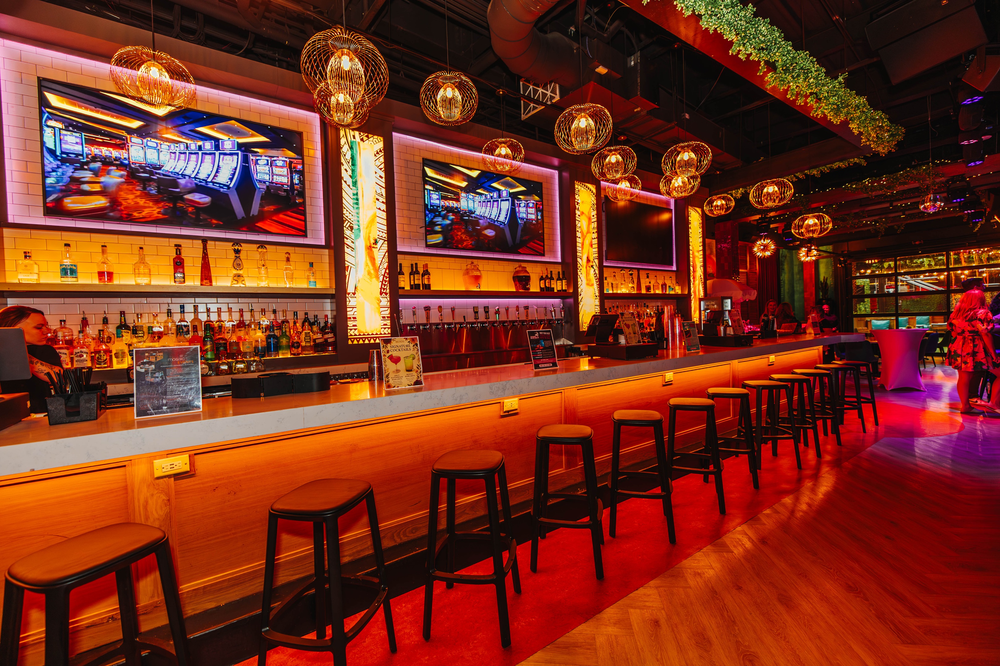 Bar seating at Besos with vibrant lighting and TV screens.