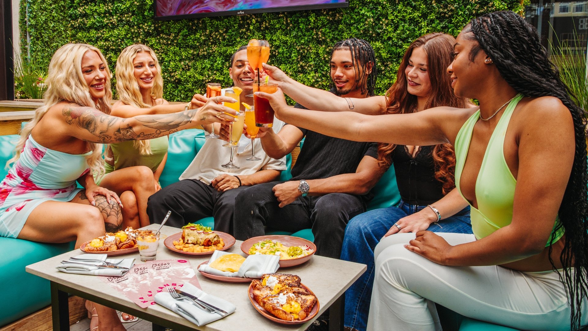Several guests at a patio table doing a cheers with their brunch cocktails.