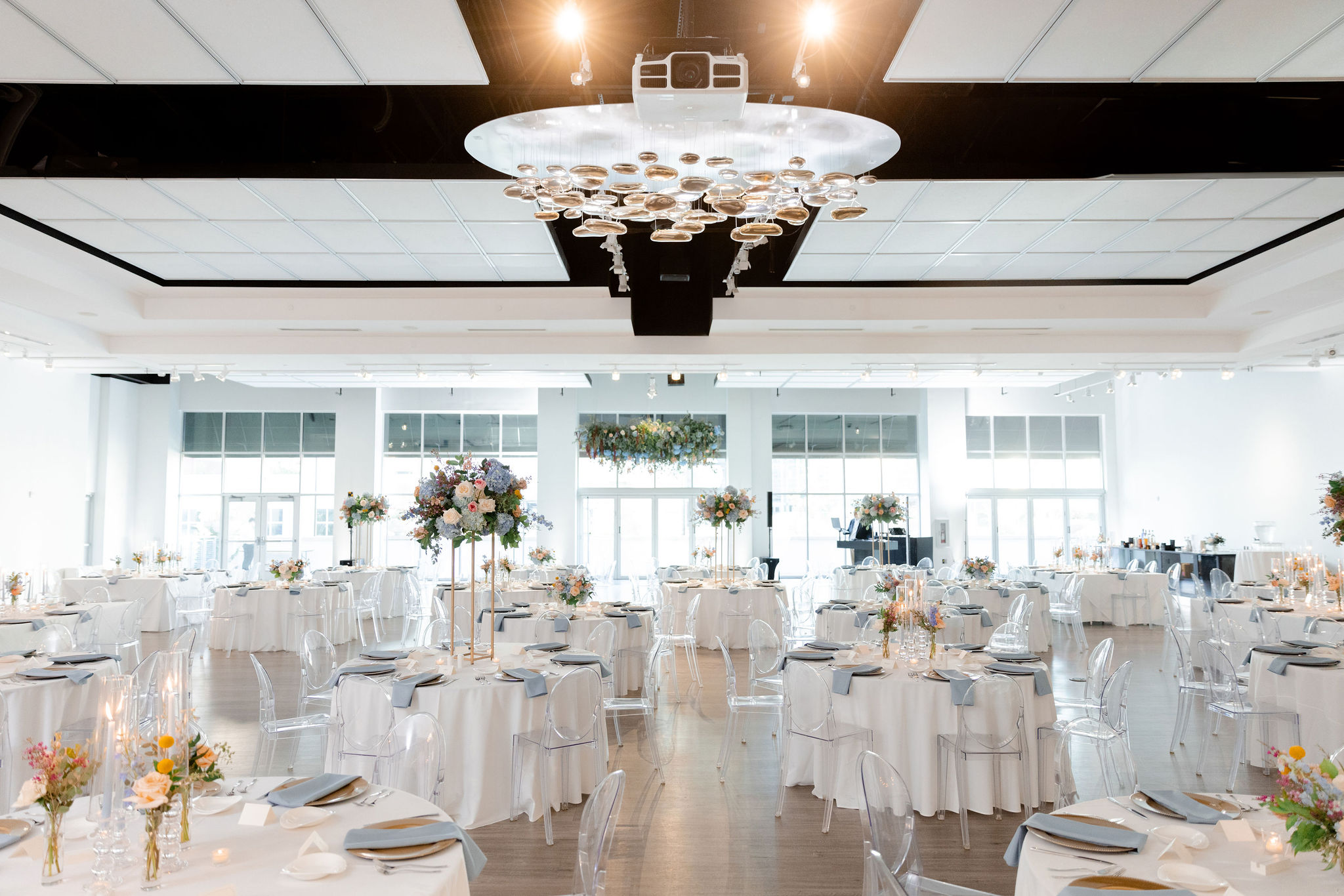 An elegant wedding setup in The Gallery featuring white linens and large green florals.