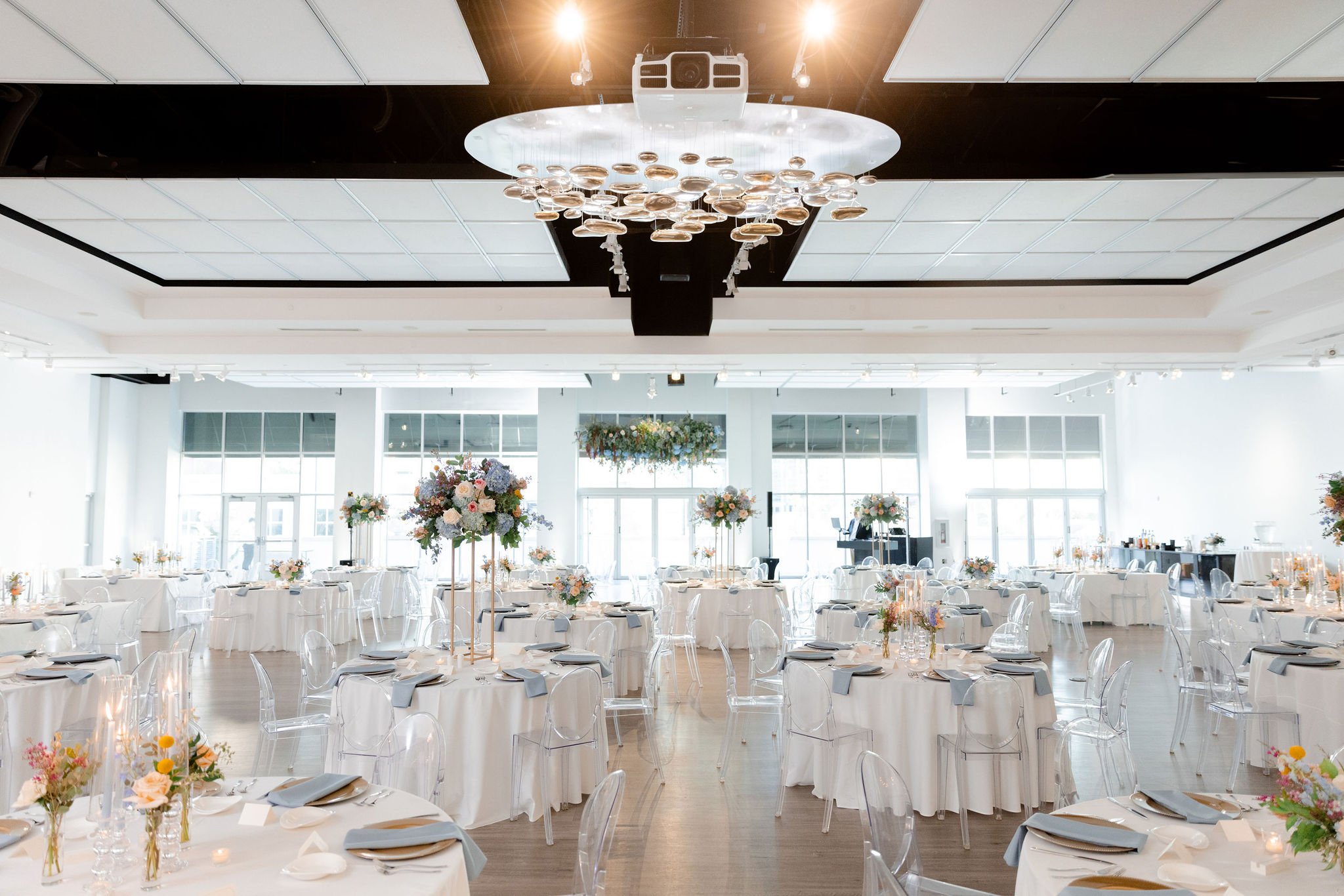An elegant wedding setup in The Gallery featuring white linens and large green florals.