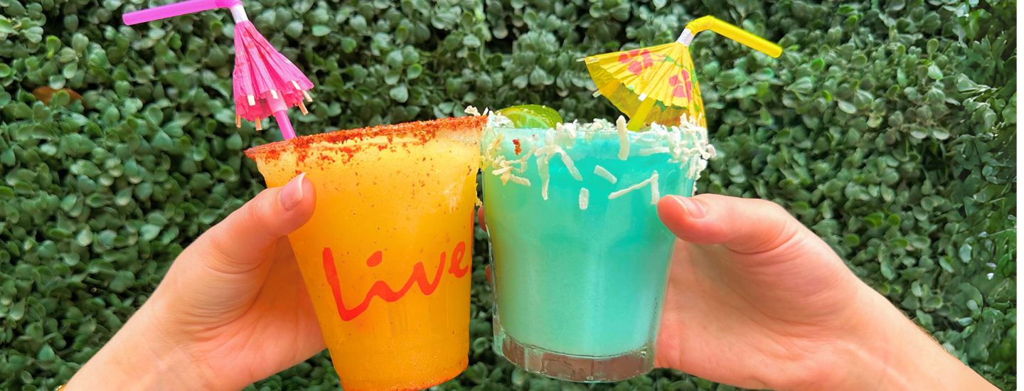 Two margaritas with tiny umbrellas being toasted.