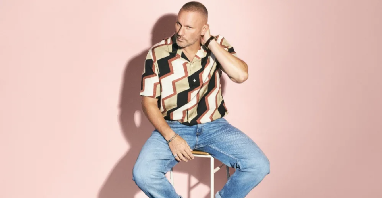Mark Knight sitting on a stool against a pink backdrop.