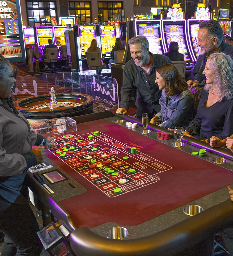 players around a roulette table, dealer stands on the other side