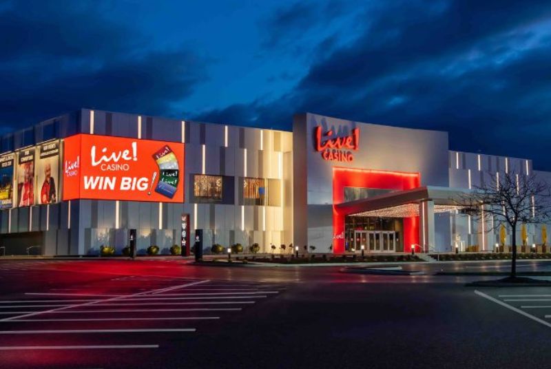 At night, the outside of the Live! Casino is lit up with vertical white lights inset against a light and dark gray exterior. 