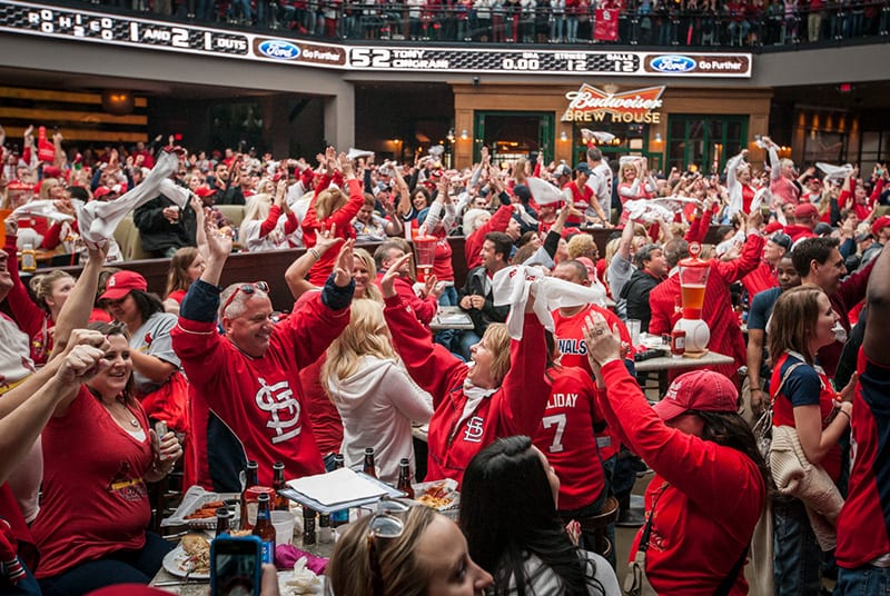 A full house of St. Louis Cardinal fans cheer, wave rally towels, and high five after a great play at Bally Sports Live!