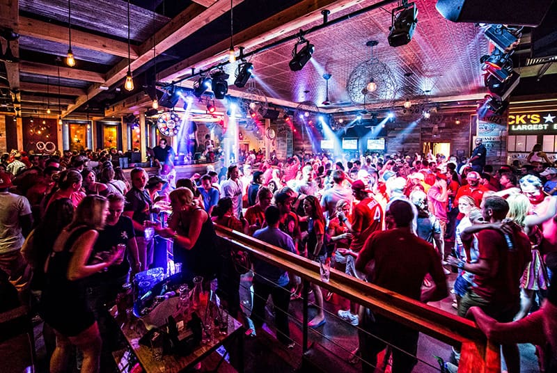 Spotlights shine on a full dance floor as friends visit over drinks at tables inside a PBR Bar.