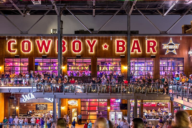 A two-story view of a PBR Cowboy Bar - from its busy balconies and wall of windows into its filled bars and tables.