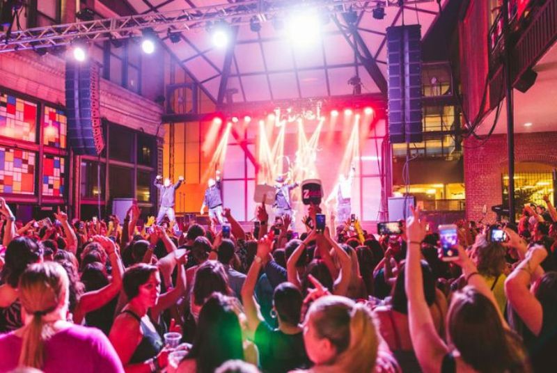 Four male singers encourage the crowd as a roomful of excited concertgoers dance and put their hands in the air at Power Plant Live!