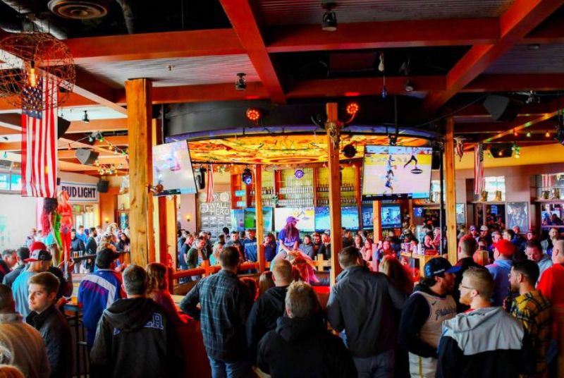 Inside a busy PBR Philly bar, a large crowd gathers around as a woman prepares to ride the mechanical bull.