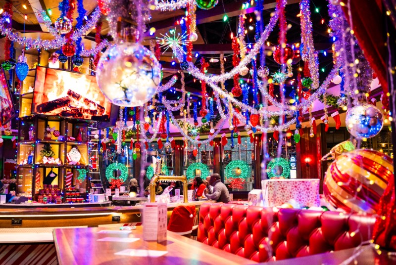 Bar and dining area decorated for the holidays with large ornaments, tinsel, and garland hanging from the ceiling.