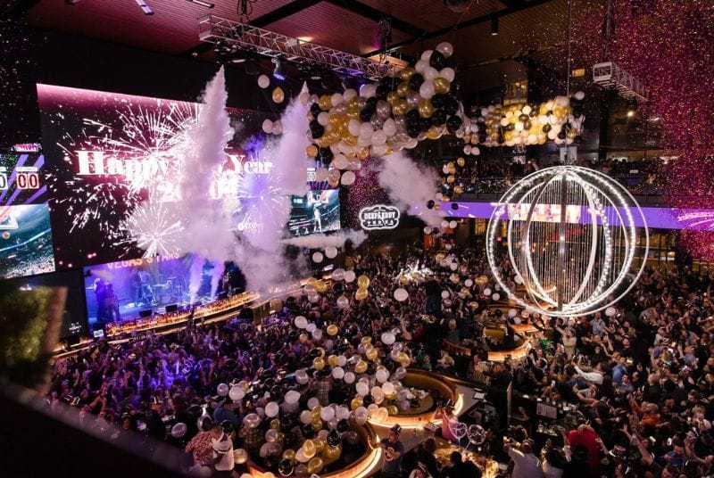 Sparkling confetti and dozens of balloons drop on a beautiful venue full of New Year's Eve partiers as midnight arrives!