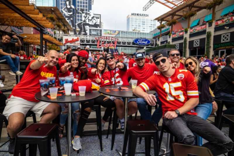 Kansas City Chiefs fans are wearing their jerseys, smiling and pointing toward the camera as their team takes on the Eagles!