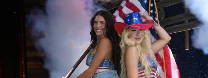 image of two girls wearing red white and blue striped shirts on a mechanical bull with smoke in the background