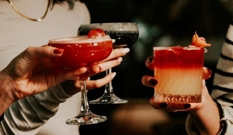 image of three hands holding festive holiday cocktails in short glasses