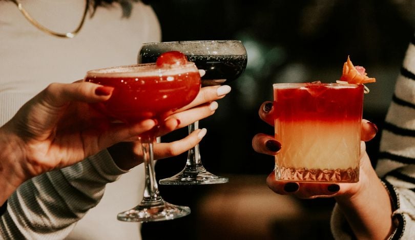 image of three hands holding festive holiday cocktails in short glasses