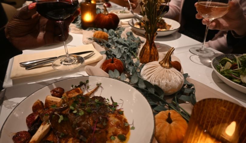 image of a fall harvest dinner with wine, roasted meats, table greenery, and a table cloth