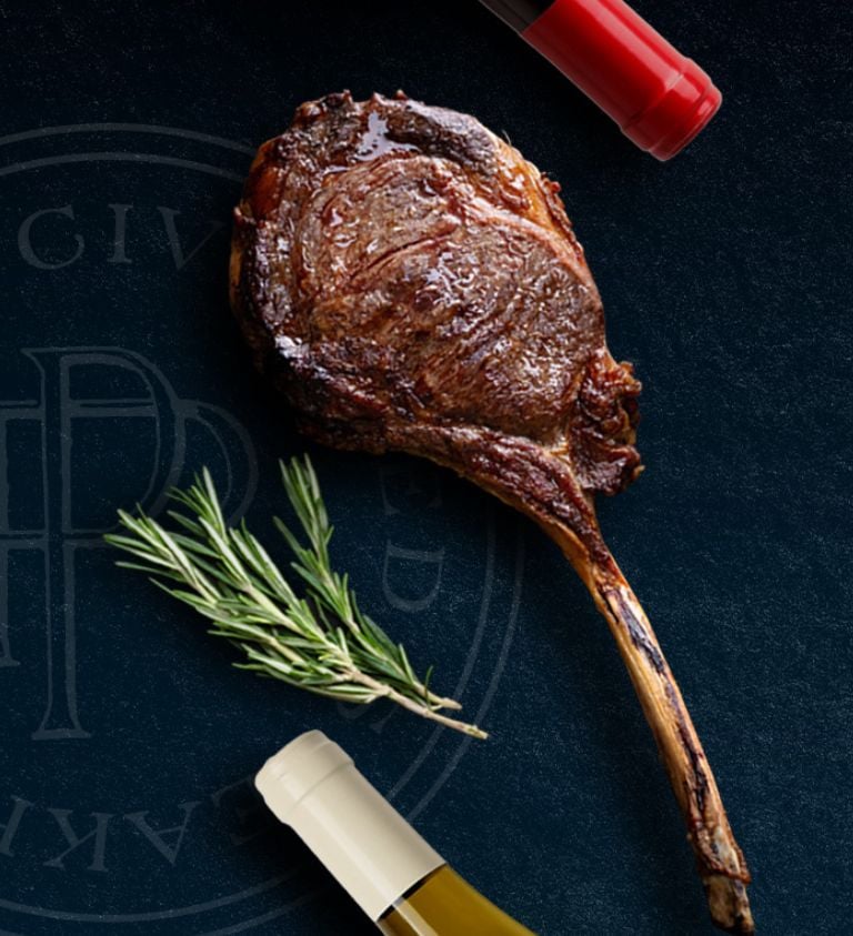 image of blue background with wagyu tomahawk steak, a sprig of rosemary, and two bottles of wine