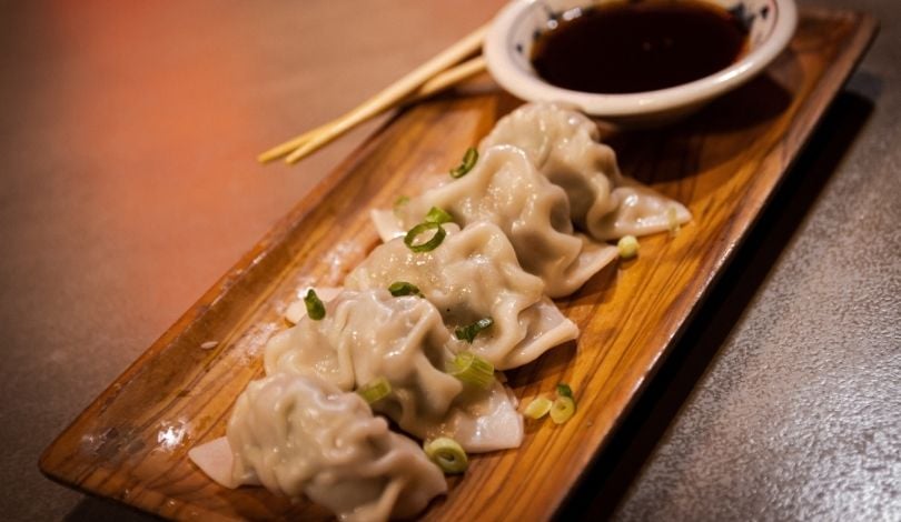 image of 5 steamed dumplings on a wooden dish next a bowl of soy sauce