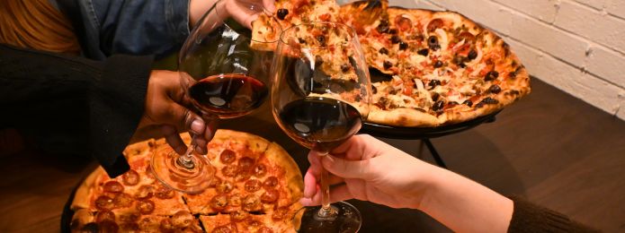 image of two pizzas at ridotto cafe with people clinking wine glasses in front of them