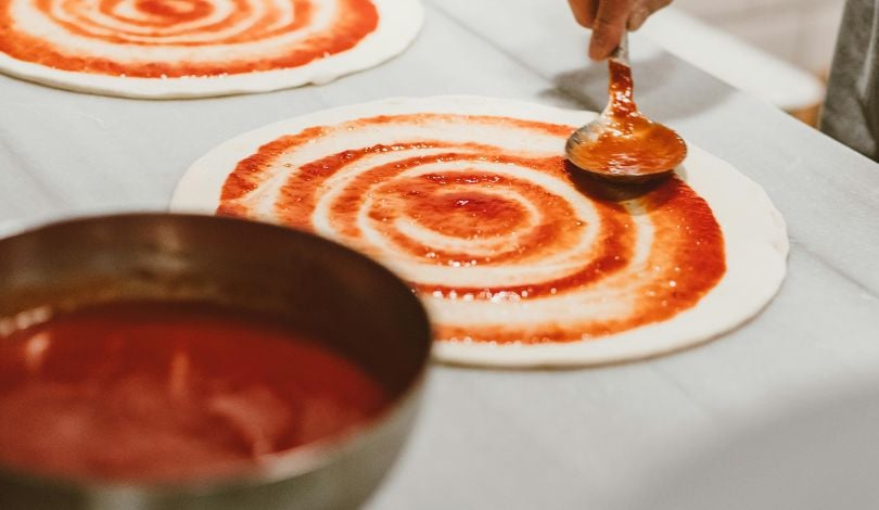 image of someone putting sauce on pizza dough with a ladle