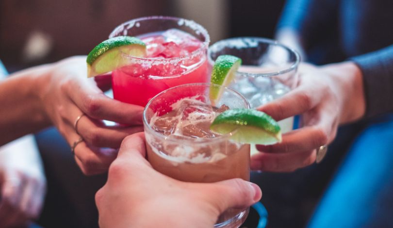 image of three people holding margarita glasses with lime garnishes
