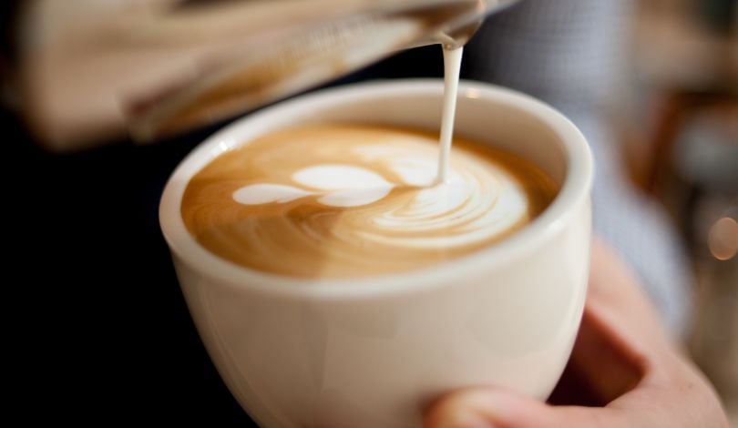 image of milk being poured into a white coffee mug with coffee in it