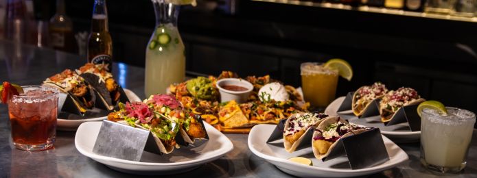 image of 4 plates of tacos at sports & social with margaritas, beer, and nachos on the table too
