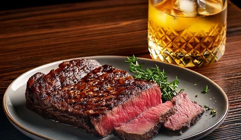 image of wagyu on a green plate next to a bourbon in a small glass