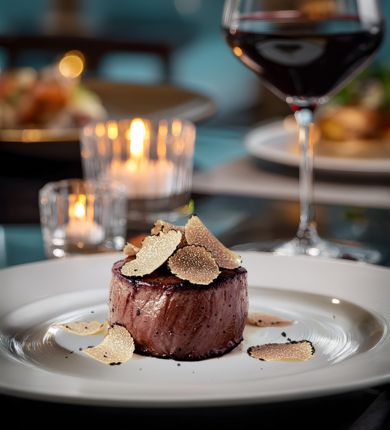 image of steak with truffle shavings on top of it next to a glass of wine