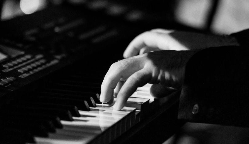 a black and white image of hands on a piano pressing on the keys