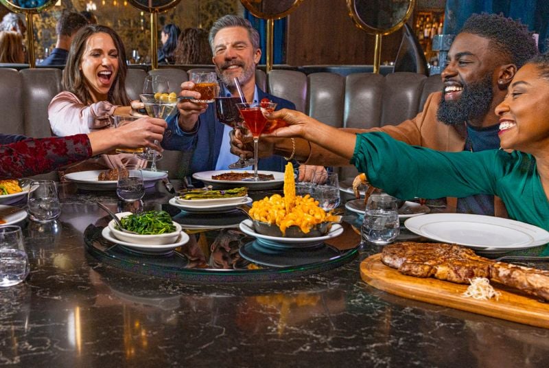 Three couples who are having dinner at The Prime Rib and are toasting their drinks.