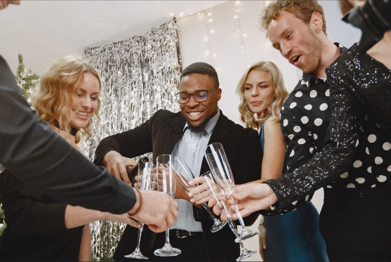 Three people in semi formal attire pouring champagne while looking excited