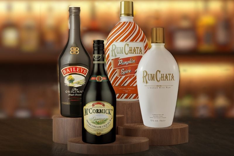 November Tuesdays on the Rocks. 4 different types of liquor sitting on wooden stands with a blurry bar background.