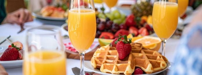 Golden waffles topped with fresh strawberries served alongside sparkling mimosas at a Father’s Day brunch table setting.