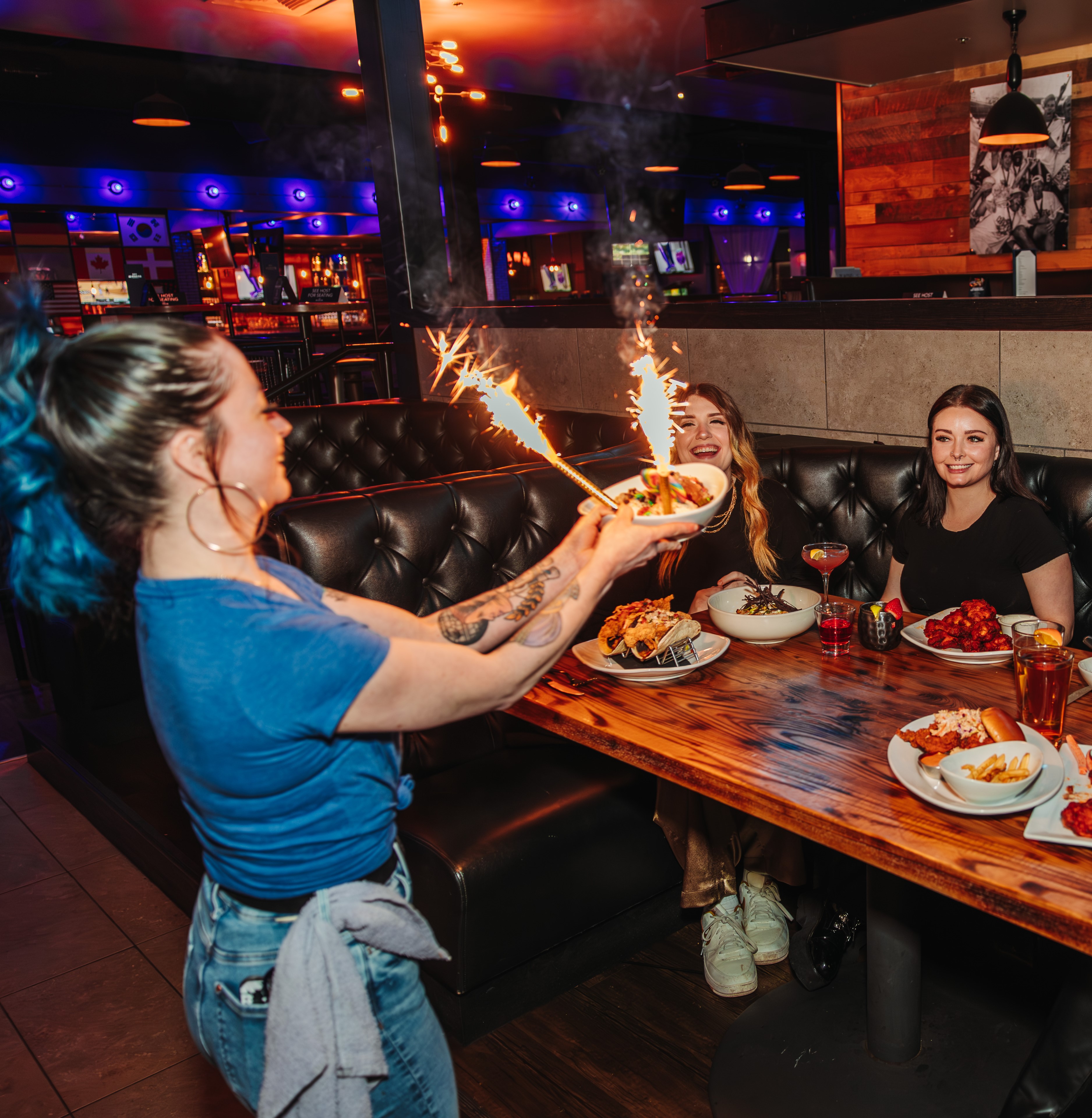 Waitress with sparklers serving two women at table.
