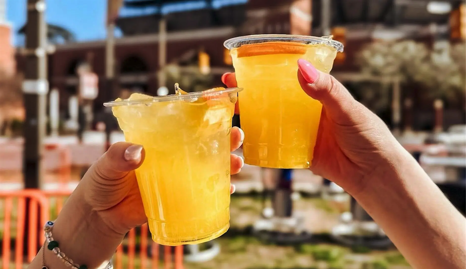 Two people holding bright yellow cocktails outdoors during a daytime event.