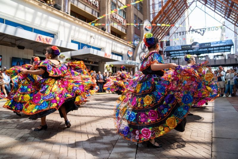 A Cinco de Mayo dance troupe performs in brightly-colored floral and lace dresses with matching flowers in their hair!