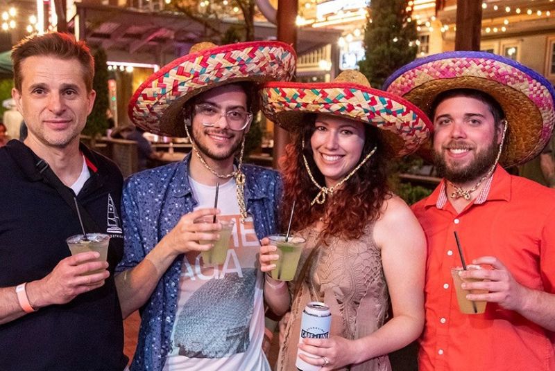 Four smiling Cinco de Mayo fans - three of whom wear sombreros - raise margaritas to toast the holiday!