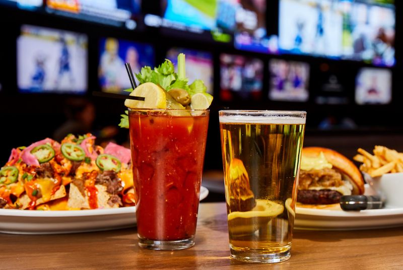 A mouth-watering plate of loaded nachos sits beside a juicy burger and fries. A tasty cocktail and beer accompany them.