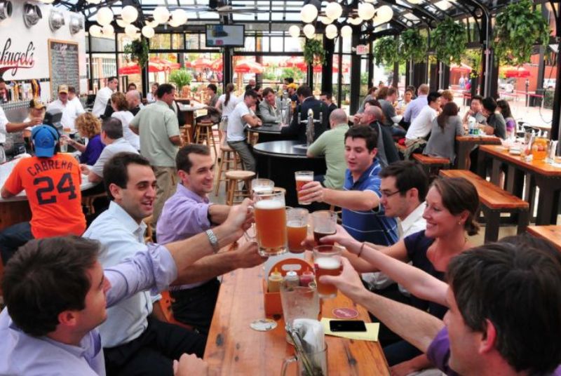 A happy table of young professionals raises beer glasses in a toast inside a busy Leinenkugel's restaurant.