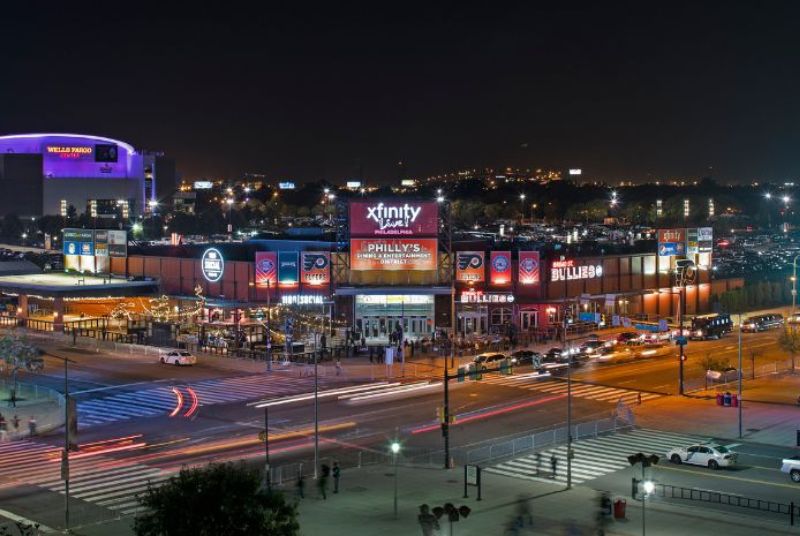 A time-lapse view of car lights and the neon signs of Xfinity Live! Philadelphia, including a purple Wells Fargo Center.