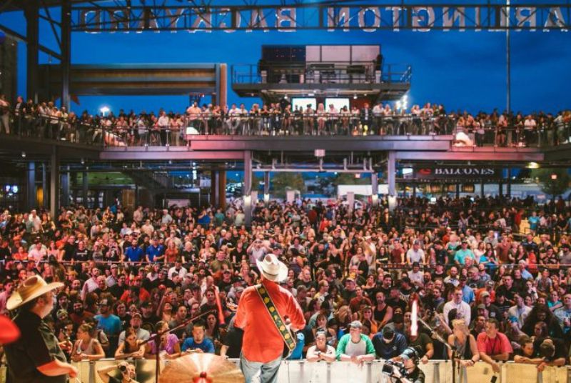 An enthusiastic crowd watches from the floor and balcony of Arlington Backyard as country performers engage them from the stage.